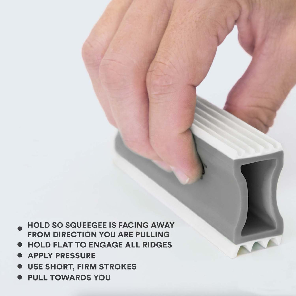 Close up of person holding the FurDozer correctly. Tips on screen read: Hold so squeegee is facing away from the direction you are pulling, hold flat to engage all ridges, apply pressure, use short, firm strokes, and pull towards you.