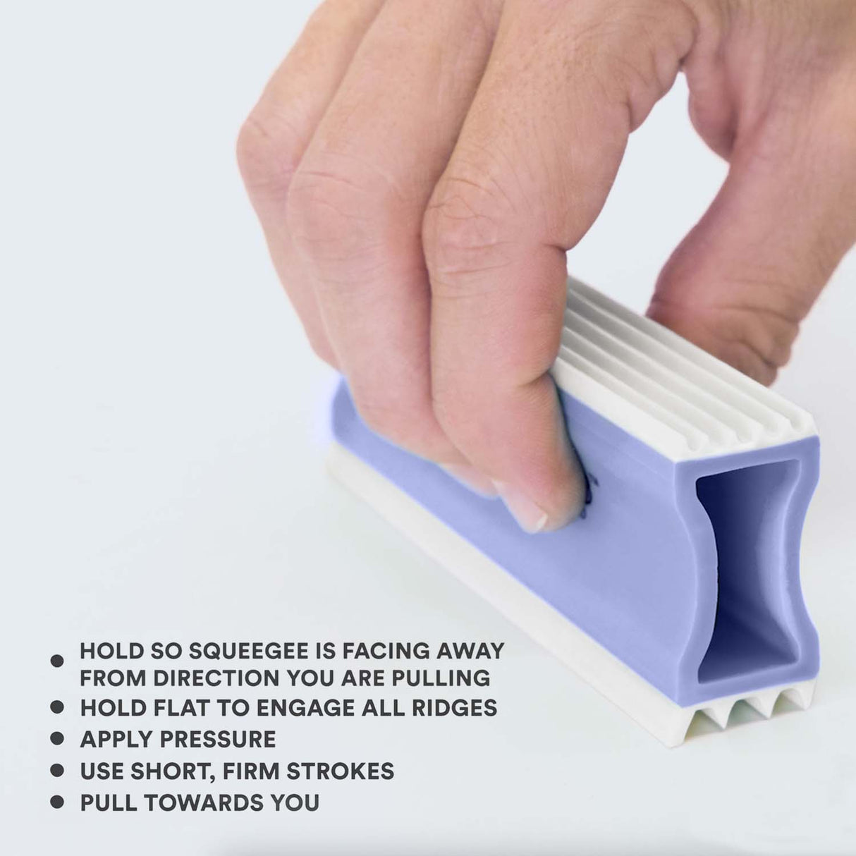 Close up of person holding the FurDozer correctly. Tips on screen read: Hold so squeegee is facing away from the direction you are pulling, hold flat to engage all ridges, apply pressure, use short, firm strokes, and pull towards you.