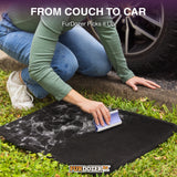 A person kneels on grass next to a car tire, using a FurDozer pet hair remover on a black car mat covered with white fur and debris. Text at the top reads 'FROM COUCH TO CAR FurDozer Picks it Up' and the FurDozer logo appears at the bottom.