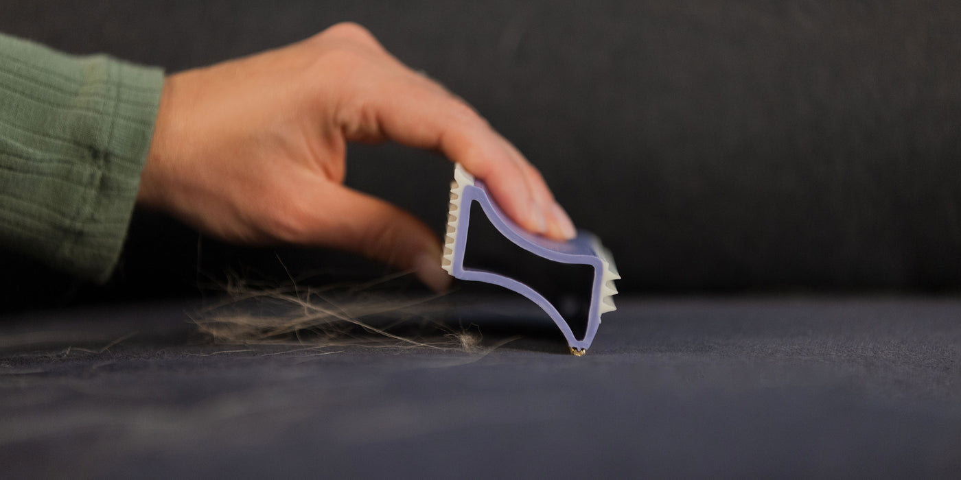 A woman uses the metal bar of the FurDozer X4 to remove pet hair from a couch