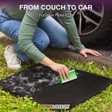 A person kneels on grass next to a car tire, using a FurDozer pet hair remover on a black car mat covered with white fur and debris. Text at the top reads 'FROM COUCH TO CAR FurDozer Picks it Up' and the FurDozer logo appears at the bottom.