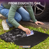 A person kneels on grass next to a car tire, using a FurDozer pet hair remover on a black car mat covered with white fur and debris. Text at the top reads 'FROM COUCH TO CAR FurDozer Picks it Up' and the FurDozer logo appears at the bottom.