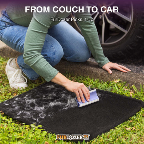 A person kneels on grass next to a car tire, using a FurDozer pet hair remover on a black car mat covered with white fur and debris. Text at the top reads 'FROM COUCH TO CAR FurDozer Picks it Up' and the FurDozer logo appears at the bottom.