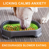 Dog licking peanut butter from the purple Neat-Lik Mat Slow Feed Licking Mat with text that reads "Encourages slow eating and reduces anxiety."